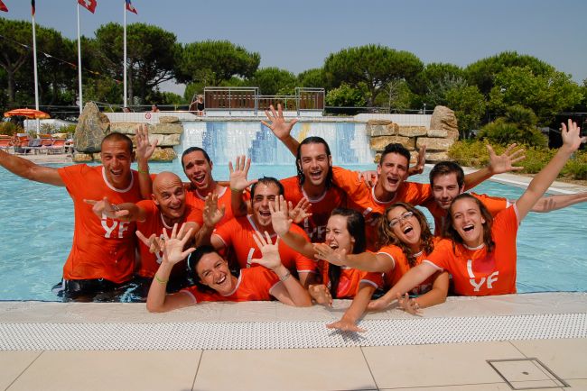 Un gruppo di persone sorridenti in magliette arancioni posa felice in una piscina.