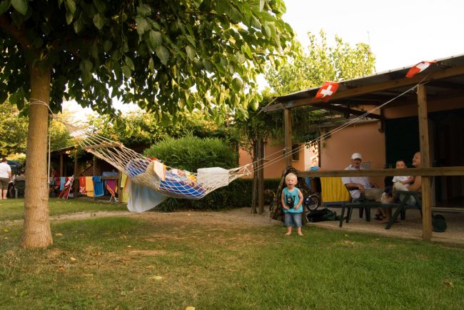 Bimbo vicino a un'amaca tra un albero e un portico.