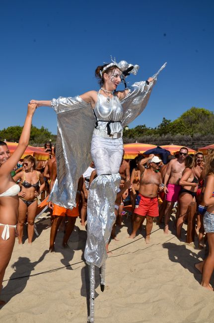 Una persona su trampoli in abito argentato sulla spiaggia.