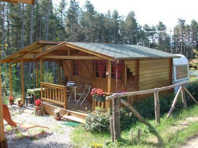 Chalet di legno con veranda e sedie, circondato da verde e alberi.