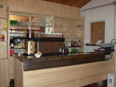 Un bancone bar in legno con bicchieri, bottiglie e una macchina da caffè.