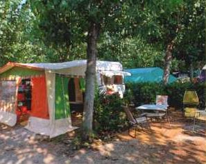 Campeggio con una roulotte, una tenda colorata e sedie sotto alberi ombrosi.
