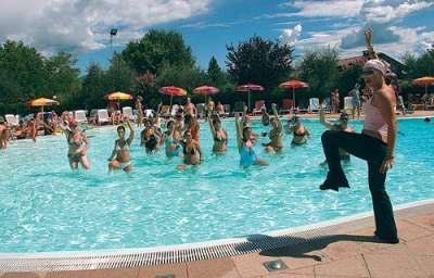 Persone che fanno acquagym in piscina con un'istruttrice in piedi.