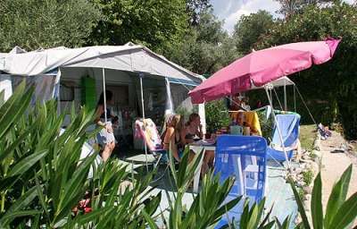 Due ombrelloni e sedie davanti a una tenda, immersi nel verde.