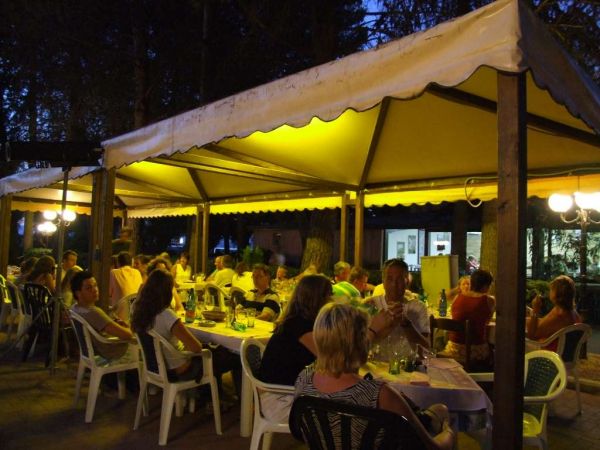 Persone sedute a tavoli sotto una tenda illuminata di notte in un ambiente all'aperto.