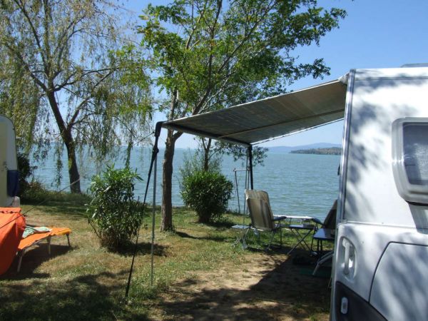 Camper con tenda affacciato su un lago. Sedie sotto l'ombra.