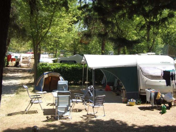 Un campeggio con roulotte, sedie pieghevoli e un tavolo sotto gli alberi.