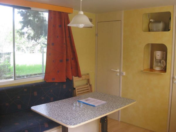 Zona pranzo con tavolo, divano e tenda rossa, luce naturale da una finestra.