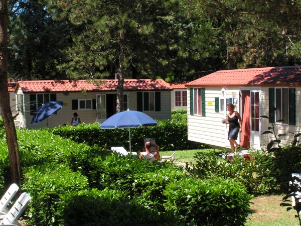 Casette con tetto rosso, persone e ombrelloni in giardino.