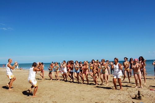 Un gruppo di persone fa esercizi in spiaggia, guidato da istruttori in tenuta bianca.
