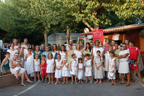 Gruppo di persone in costumi antichi davanti a un chiosco, circondati da alberi.