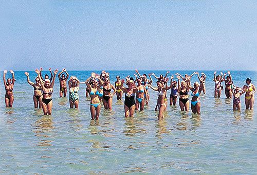 Persone sorridenti in costume fanno esercizi in mare.