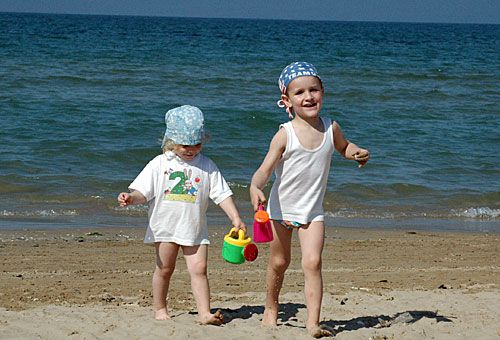 Due bambini piccoli con cappellini giocano sulla spiaggia vicino al mare.
