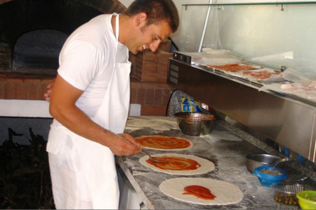 Uomo prepara delle pizze in una cucina.