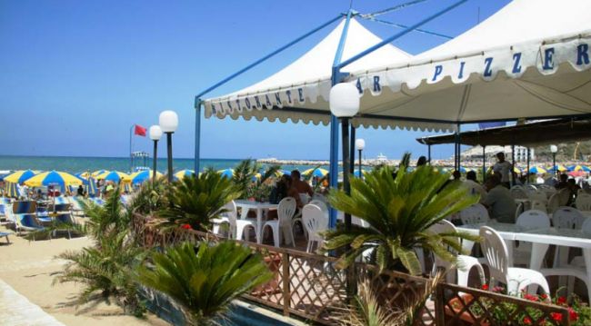 Ristorante sulla spiaggia con tavoli bianchi.