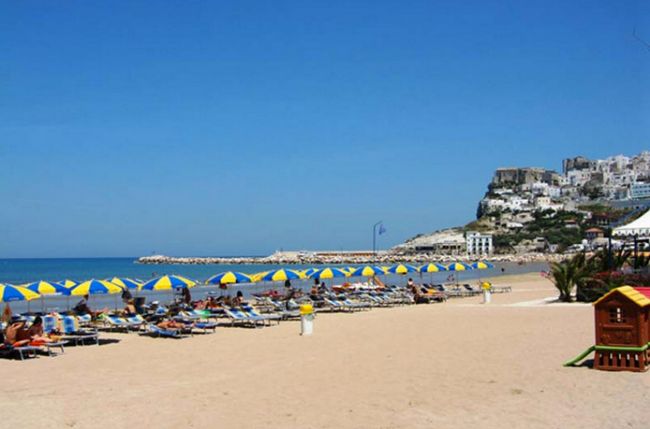 Spiaggia sabbiosa con lettini e ombrelloni gialli e blu.