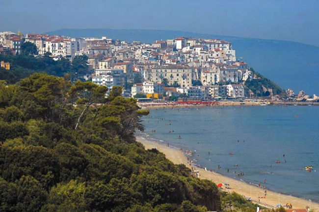 Vista su una spiaggia con città collinare e bagnanti in acqua.