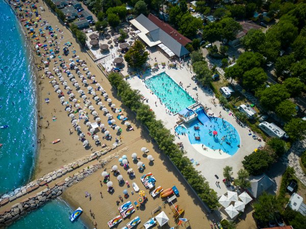 Piscina accanto a una spiaggia affollata con ombrelloni.