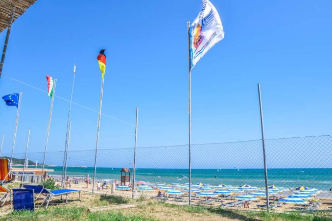 Spiaggia con bandiere e ombrelloni colorati.