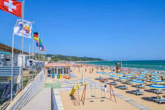 Vista della spiaggia con bandiere e ombrelloni blu.