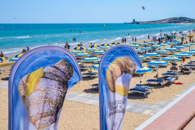 Spiaggia affollata con ombrelloni blu e gialli vicino al mare.