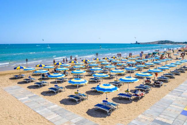 Ombrelloni blu e gialli in fila su una spiaggia soleggiata.