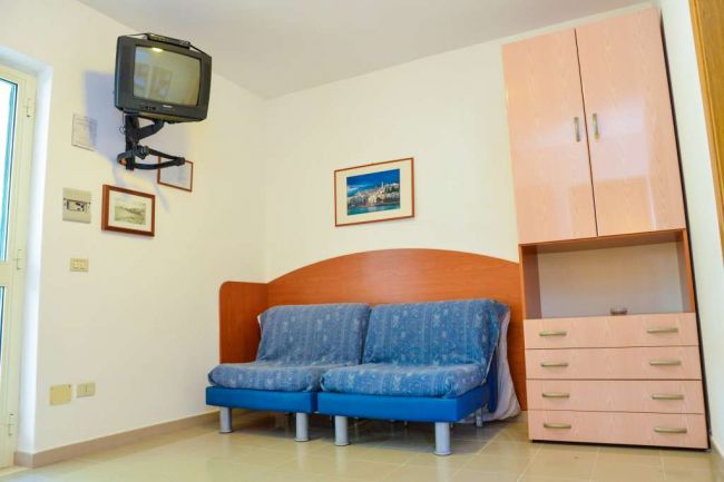 Stanza con divano blu, TV sospesa e armadio.