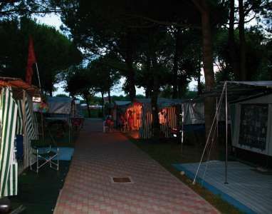 Sentiero in un campeggio, circondato da tende illuminate da luci rossastre al crepuscolo.