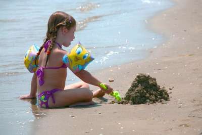 Bambina con braccioli gioca con la sabbia vicino al mare.