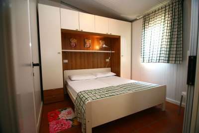 Camera da letto con letto matrimoniale, armadio bianco e finestra con tenda a quadri.