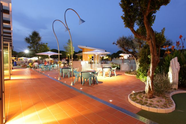Patio con tavoli e sedie illuminato di sera.