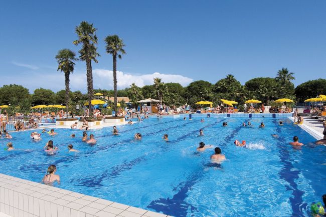 Piscina affollata con palme e ombrelloni gialli.