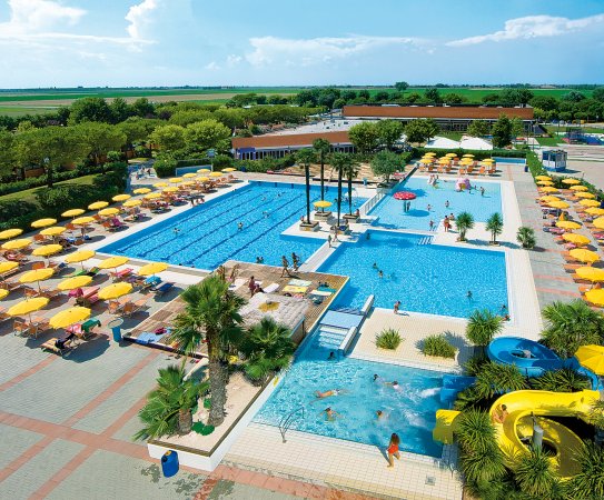 Piscina con scivolo, ombrelloni gialli e verde intorno.