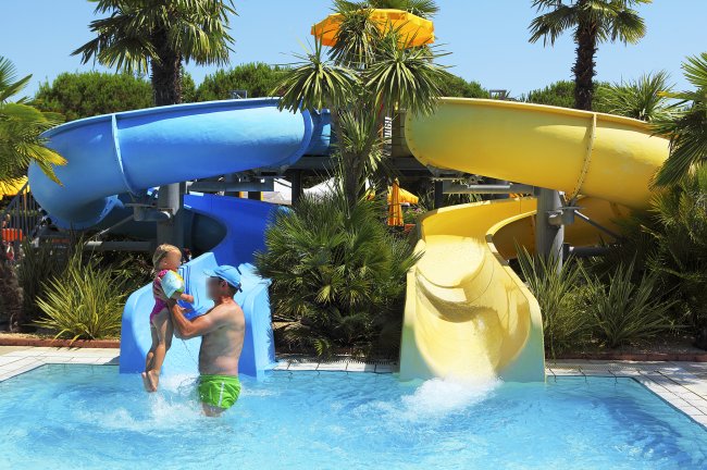 Una piscina con scivoli blu e gialli e persone che giocano.