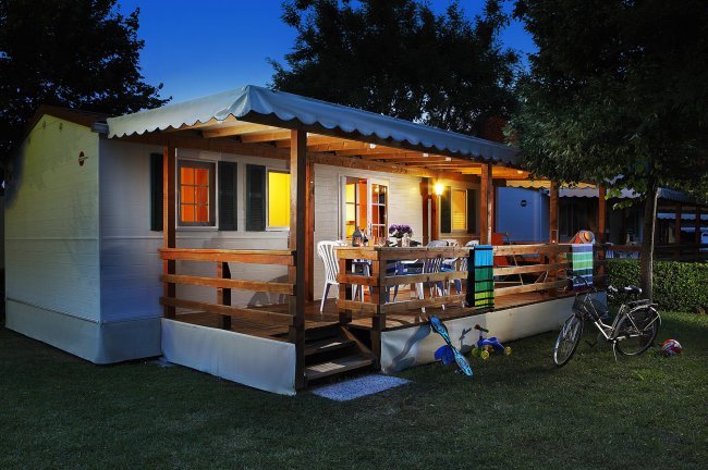 Una casa mobile illuminata con veranda, tavolo, sedie e biciclette.
